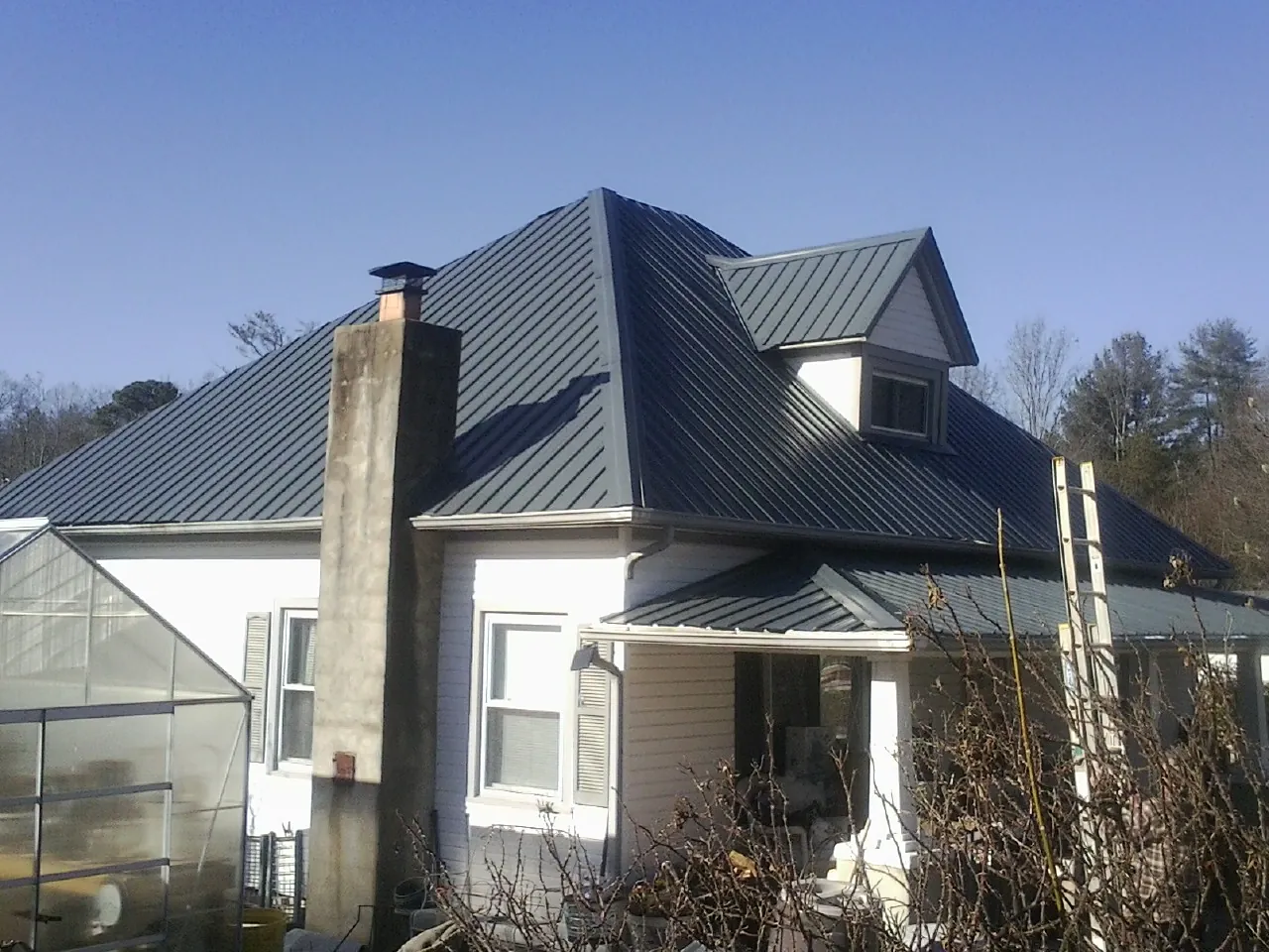 Dark blue standing seam metal roof on a white farmhouse with dormer — Slate & Tile Roof Repair by Roofing Brothers in Cabot