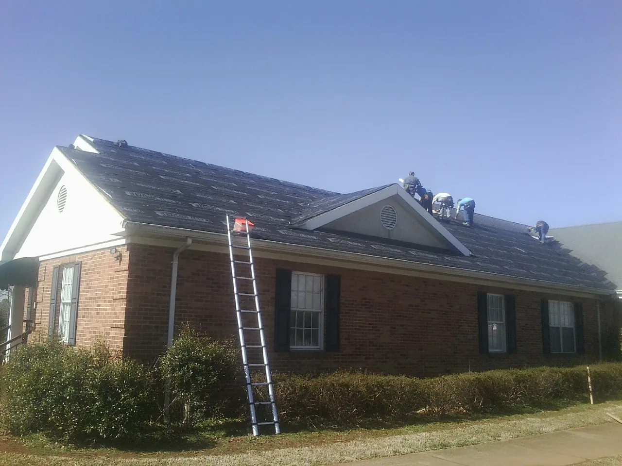 Crew tearing shingles off a brick ranch roof with a ladder set — Metal Roof Repair work by our crew in Cabot