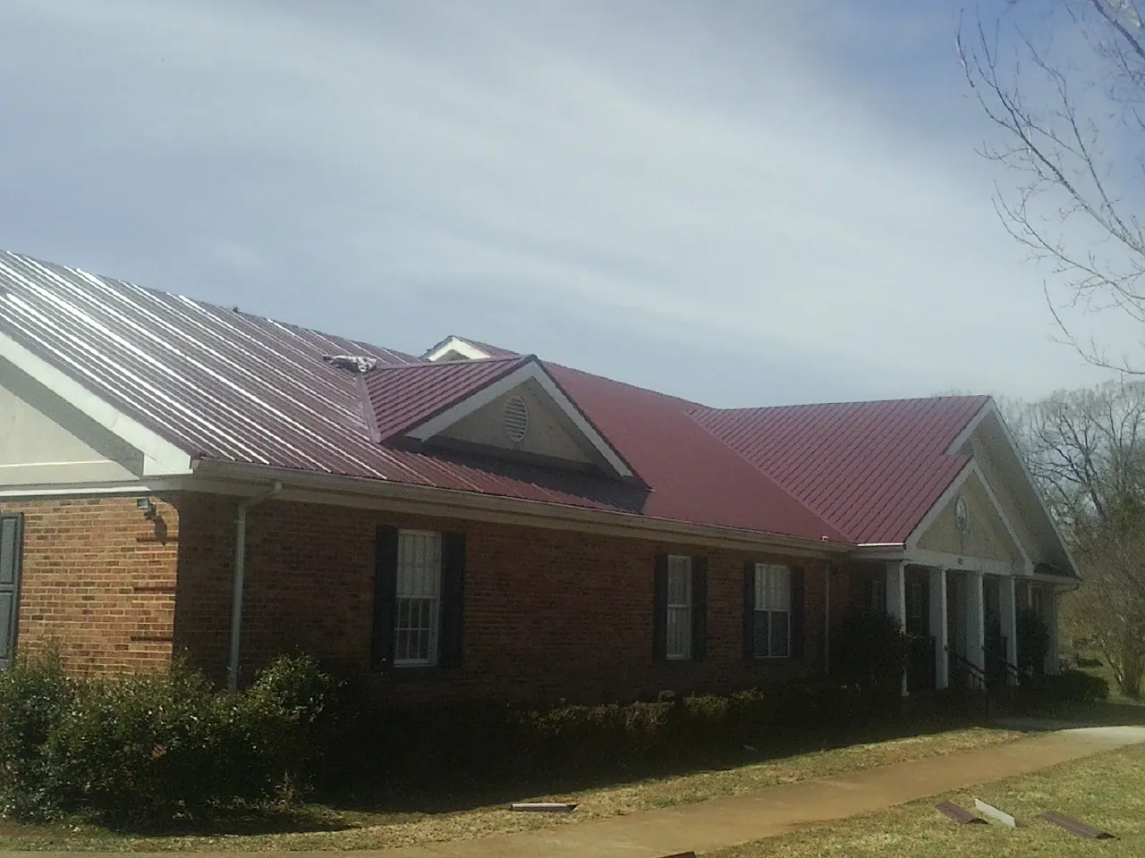 Red metal roof with gabled entries on a long brick building, from a Hail Damage Roof Repair job in Cabot