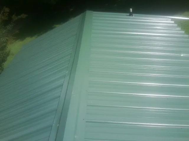 New green metal panels meeting at the ridge of a roof — Flat Roof Repair work by our crew in Cabot
