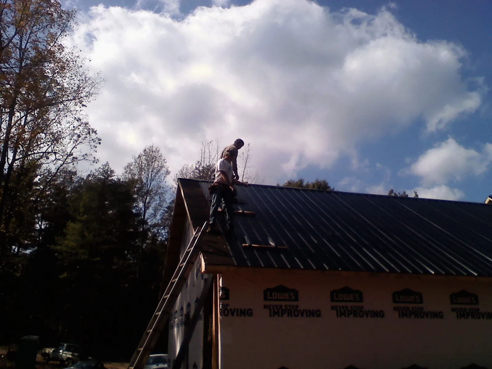 Roofer fastening dark metal panels high against a cloudy sky, from a Roof Inspection job in Cabot